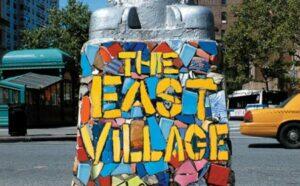 A lamp post base painted blue, red and yellow with the letters the East Village.